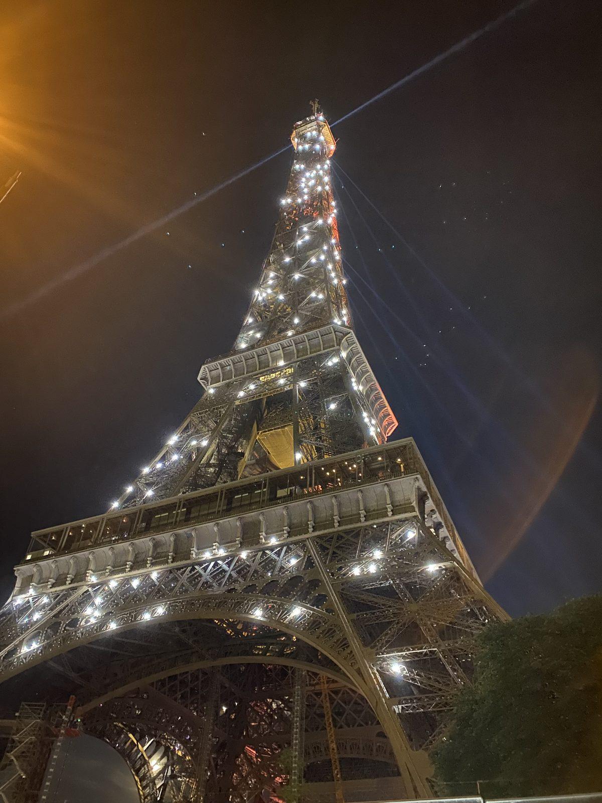 The Eiffel Tower sparkling at night behind a lit tree